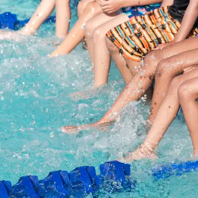 Kinder, die mit den Beinen das Wasser im Schwimmbad spritzen lassen